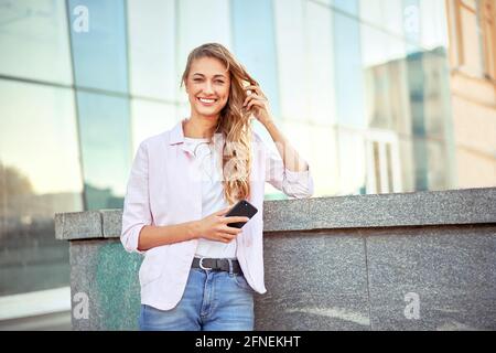 Geschäftsfrau steht Sommertag in der Nähe von Firmengebäude mit Smartphone Zähne Lächelnde Geschäftsfrau im Freien erfolgreiche europäische kaukasische Frau Stockfoto