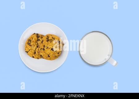 Zwei amerikanische Kekse auf weißer Porzellanuntertasse und eine transparente Tasse Milch auf blauer Oberfläche. Draufsicht. Stockfoto