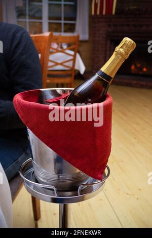 Flasche Champagner im Eiskübel aus Metall mit rotem Handtuch auf dem Ständer im Inneren des Restaurants. Stockfoto