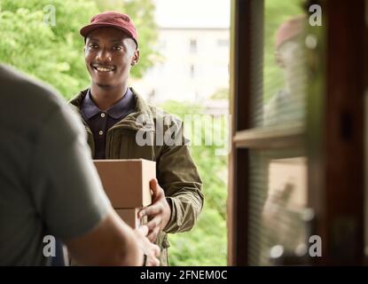 Lächelnder afrikanischer Kurier, der Pakete an einen Kunden liefert Stockfoto
