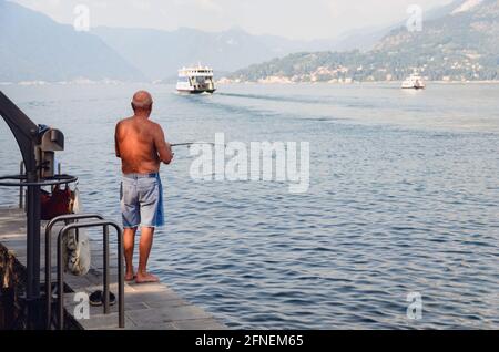 Alter Mann von hinten gesehen und Angeln am Ufer des Comer Sees, Italien, in weichem frühen Morgensonne Stockfoto