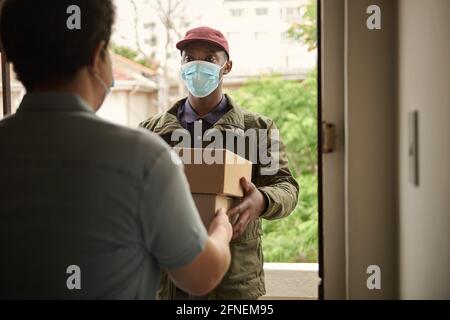 Afrikanischer Kurier in einer Maske, der Pakete an einen Kunden liefert Stockfoto