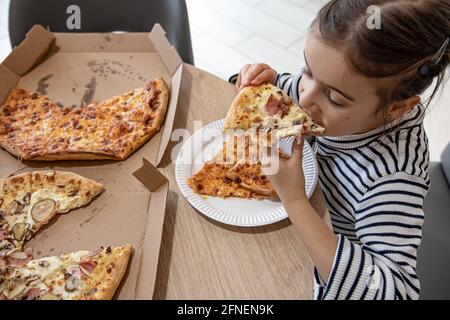 Ein süßes kleines Mädchen isst appetitlich ein Stück Pizza zum Mittagessen. Stockfoto