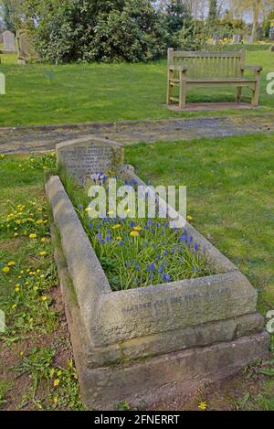 Frühlingsblumen umgeben Grabsteine auf dem Kirchhof in der St. Peter's Church, Chelmarsh, Shropshire, Großbritannien Stockfoto