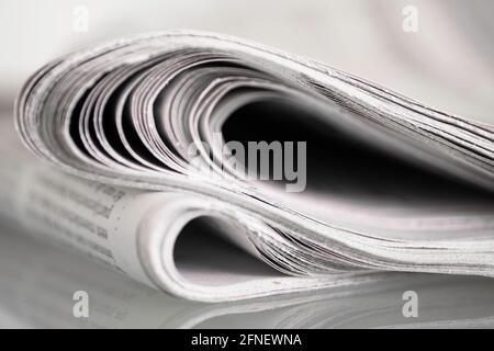 Zwei gefaltete Zeitungen, die auf einem Glastisch vor schlichtem Hintergrund gespiegelt wurden Mit geringer Schärfentiefe Stockfoto