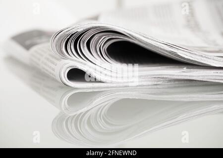 Gefaltete Zeitung auf Glastisch vor schlichtem Hintergrund mit enger Schärfentiefe gespiegelt Stockfoto