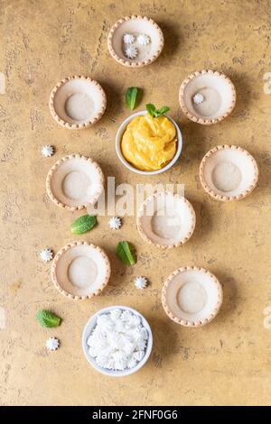 Leere Shortbread-Tartlets, Zitronenkurz, Mini-Bagues und Minze auf betontem Hintergrund. Verarbeiten Sie das Dessert. Selektiver Fokus. Stockfoto