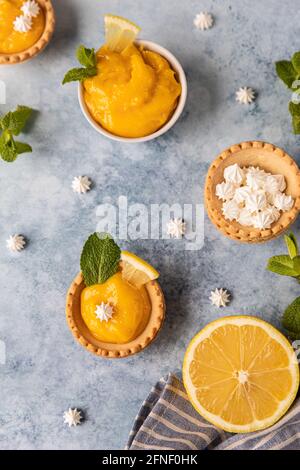 Minitörtchen mit Zitronenquark, Mini-Baiser, Zitronenscheiben und Minze auf blauem Betongrund. Draufsicht. Selektiver Fokus. Stockfoto