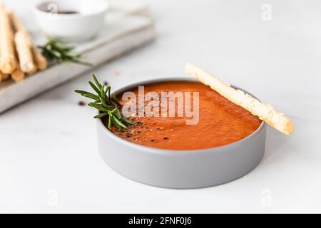 Tomatensuppe garnieren mit gemahlenem Pfeffer, Rosmarin und Brotscheiben, heller Hintergrund. Selektiver Fokus. Stockfoto