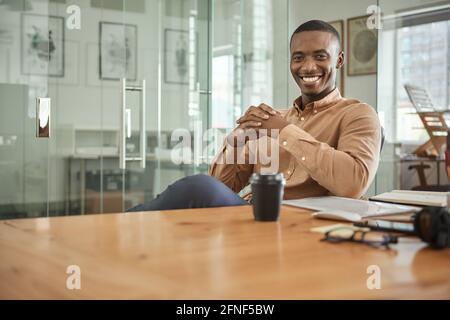 Junger afrikanischer Geschäftsmann, der lächelt, während er an seinem Schreibtisch sitzt Stockfoto