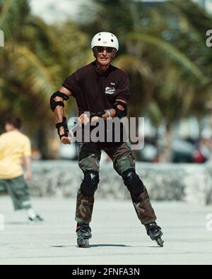 Ein älterer Mann mit Ellenbogenschützern, Knieschützern und einem Helm fährt mit seinen Rollerklingen auf der Strandpromenade von Miami Beach. [Automatisierte Übersetzung] Stockfoto