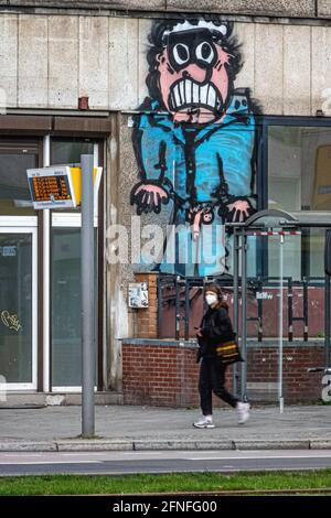 Frau mit Gesichtsmaske geht während der Covid Pandemie, Mitte, Berlin, an einer Bushaltestelle vorbei. Straßenkunst von gruselig gesichtigen Blinker an der nahe gelegenen Wand Stockfoto