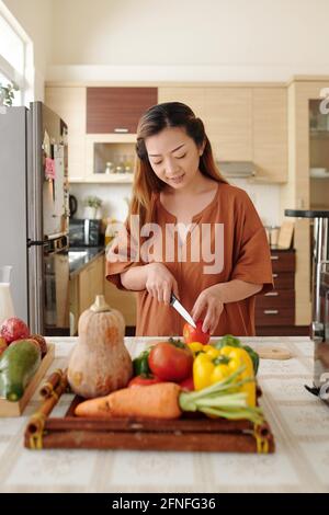 Hübsche junge Frau, die das Abendessen macht, schneidet frisches Gemüse am Küchentisch Stockfoto