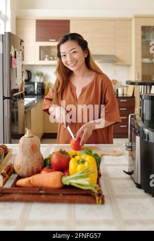 Porträt einer lächelnden, hübschen jungen Frau, die gerne kocht, schneidet Gemüse für Salat Stockfoto