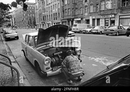 Ein Mann repariert seinen Trabant 601 am Straßenrand in Berlin-Prenzlauer Berg. Um den Motor leichter erreichen zu können, konnte die Kühlerhaube des Trabant einfach entfernt werden. [Automatisierte Übersetzung] Stockfoto