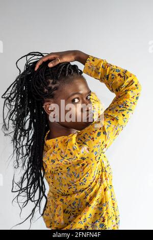 Seitenansicht des afroamerikanischen weiblichen Modells mit Zöpfen, die sich berühren Haare beim Betrachen der Kamera auf grauem Hintergrund im Studio Stockfoto
