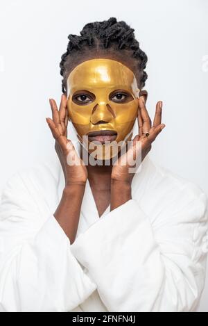 Schwarze Frau in goldenen Blatt Maske tun Hautpflege Behandlung auf Weißer Hintergrund im Badezimmer Stockfoto