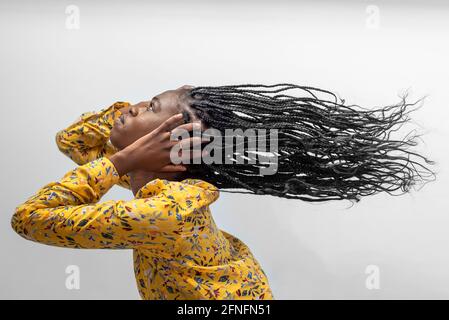 Seitenansicht einer sorglosen afroamerikanischen Hündin mit langem Fliegen Geflochtene Haare auf grauem Hintergrund Stockfoto