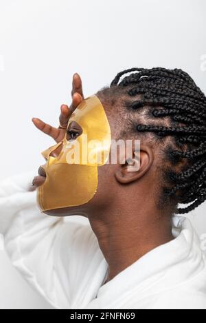 Schwarze Frau in goldenen Blatt Maske tun Hautpflege Behandlung auf Weißer Hintergrund im Badezimmer Stockfoto