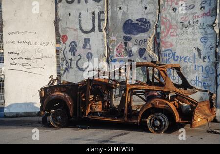 Vor den Resten der Berliner Mauer brannte Trabant aus. Fotografie um 1991 [automatisierte Übersetzung] Stockfoto