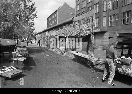 Berlin-City / Bezirke / Kreuzberg / DDR / 1990 Mitte 1990 ist die Mauer bereits sehr stark beschädigt. Spechte haben überall Stücke ausgeschlagen, wie hier in der Zimmerstraße. DDR-Flagge beim Hausierer. // Berliner Mauer / DDR-Mauer / Geschichte / Kommunismus [automatisierte Übersetzung] Stockfoto