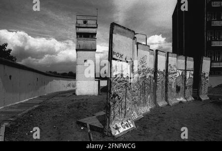 Berlin-Bezirke / DDR / Anfang 1990 Kreuzberg / Treptow: Mauerabriss in Treptow, Todesstreifen und Wachturm. Teile der Wand warten darauf, weggenommen zu werden. Solche Elemente werden verkauft, wenn sie lackiert werden. Aber in diesem Fall haben die Wandspechte bereits die besten Stücke herausgeschlagen. Hinter der Mauer liegt Kreuzberg // Mauer /Bezirke / Geschichte / Kommunismus [automatisierte Übersetzung] Stockfoto