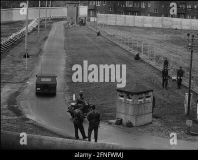 Berlin-Neukoelln / DDR / Mauer / 10 / 1980 DDR-Grenzposten ziehen neuen Stacheldraht entlang der Mauer, der Bouchestrasse zwischen Neukoelln und Treptow. Es wird elektrisch geladen und löst bei Berührung einen Alarm aus. Oben links befindet sich West-Berlin. Die Wand ist weiß gestrichen, um Flüchtlinge hervorstechen zu lassen. Die beiden Grenzposten davor achten darauf, dass die anderen nicht in den Westen fliehen. // Stacheldraht / Grenzbefestigungen / Bezirke [automatisierte Übersetzung] Stockfoto