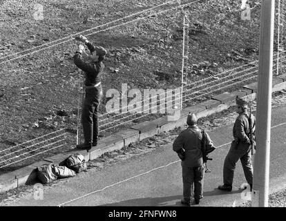 Berlin-Neukoelln / DDR / Mauer / 10 / 1980 DDR-Grenzposten ziehen neuen Stacheldraht entlang der Mauer, der Bouchestrasse zwischen Neukoelln und Treptow. Es wird elektrisch geladen und löst bei Berührung einen Alarm aus. Oben links befindet sich West-Berlin. Die Wand ist weiß gestrichen, um Flüchtlinge hervorstechen zu lassen. Die beiden Grenzposten davor achten darauf, dass die anderen nicht in den Westen fliehen. // Stacheldraht / Grenzbefestigungen / Bezirke [automatisierte Übersetzung] Stockfoto