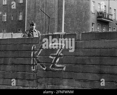 Berlin-City / DDR / 20.3.1980 Bernauer Straße in Wedding. Die alten Wandsteine werden durch L-förmige Elemente aus glattem Beton ersetzt. Der junge Grenzposten steht dort, um die Bauarbeiter zu bewachen. Um zu verhindern, dass sie in den Westen fliehen. Auf der Westseite hat jemand -KZ- an die Wand geschrieben. Hinter der Mauer befindet sich Berlin-Mitte. // DDR / Mauer / Bezirke / Stasi / Geschichte / Kommunismus [automatisierte Übersetzung] Stockfoto