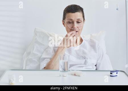 Ältere Frau liegt auf dem Bett und nimmt im Krankenhaus Pillen ein Stockfoto