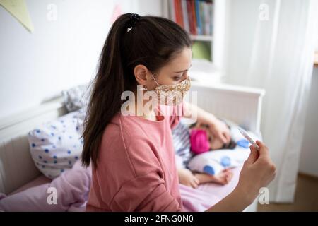 Mutter, die sich um kranke kleine Tochter im Bett zu Hause, Coronavirus Konzept. Stockfoto