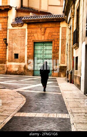 Touristischer Spaziergang durch die San Juan de Dios Straße in Murcia. Fassade aus geschnitztem Stein und alte Holztür an der Kirche San Juan de Dios. Stockfoto