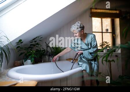 Draufsicht auf eine ältere Frau im Badezimmer, die sich zu Hause auf ein Bad vorbereitet. Stockfoto