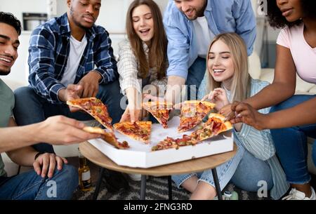 Glückliche multirassische Freunde plaudern, gemeinsam Pizza essen, eine kleine Party zu Hause haben Stockfoto