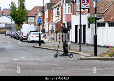 Ein junger weißer Mann, der einen Elektroroller auf dem reitet Straße in Southall London England Großbritannien Stockfoto