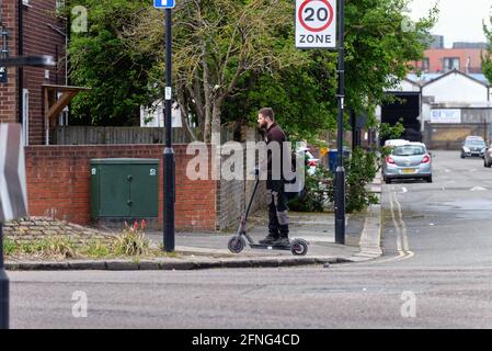 Ein junger weißer Mann, der einen Elektroroller auf dem reitet Bürgersteig in Southall London England Großbritannien Stockfoto