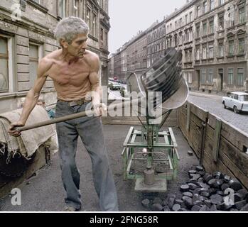 Sachsen / Orte / DDR-Land / Leipzig-Connewitz, 1990. Das Arbeiterviertel war sehr verfault und sollte nach Plänen der DDR teilweise abgerissen werden. Das Foto zeigt eine Gründerzeit Straße und den Koalman. Er liefert in den Keller. Es war üblich, die Kohlen einfach auf die Straße zu schaufeln. Foto: Kohle wird in den Kalkübel geschaufelt. Der Eimer wird dann gekippt und die Kohlen gleiten in einen Sack. // Braunkohle / Energie / Kohle / Arbeit / KW / Bundesländer / [automatisierte Übersetzung] Stockfoto