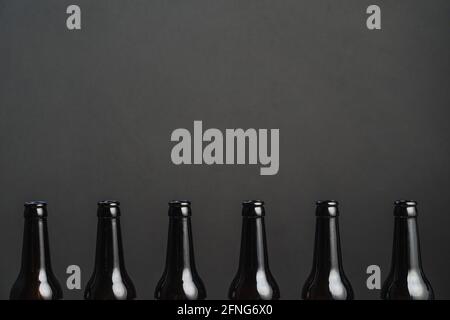 Reihe von identischen dunklen Flaschen mit alkoholischen Getränken mit glänzend Oberfläche auf grauem Hintergrund Stockfoto