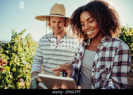 Ein vielfältiges Bauernpaar arbeitet zusammen an einem Projekt, das in Weinbergen steht Informationen auf einem digitalen Tablet recherchieren Stockfoto