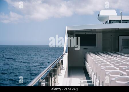 Deck des Kreuzfahrtbootes mit leeren weißen Stühlen in Reihe Unter klarem Himmel mit Wolken Stockfoto