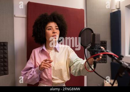 Schwarze Sängerin, die Lied gegen Mikrofon mit Pop-Filter aufführt Dabei mit der Hand auf der Hüfte stehen und nach vorne schauen Tonstudio Stockfoto