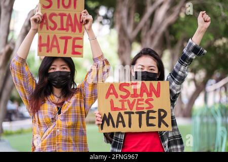 Ethnische Frauen in Masken und mit Stop Asian Hass und Asian Lives Matter Plakate, die gegen Rassismus auf der Straße protestieren Und Blick auf die Kamera Stockfoto