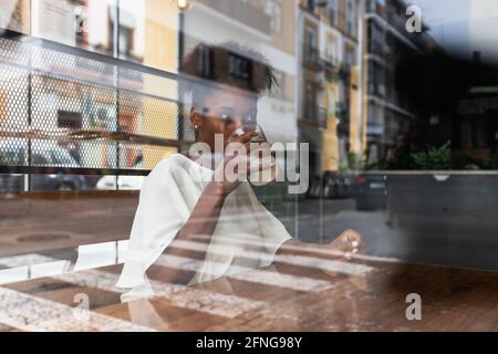 Durch Glasbauchflächen ruhige afroamerikanische Hündin in lässigem Outfit Kaltes frisches Wasser aus der Flasche in das Glas mit Eis trinken Und Zitrone beim Sitzen Stockfoto