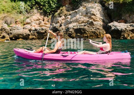 Seitenansicht Reisende mit Paddeln schwimmend auf türkisfarbenem Meerwasser in der Nähe Die felsige Küste an sonnigen Tagen in Malaga Spanien Stockfoto