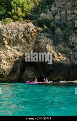 Seitenansicht anonymer Reisende mit Paddeln auf türkisfarbenem Meerwasser In der Nähe der felsigen Küste an sonnigen Tagen in Malaga Spanien Stockfoto