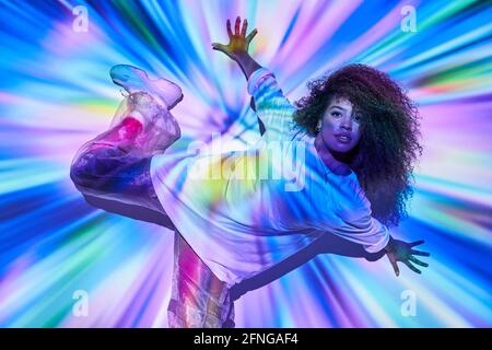 Draufsicht energische afroamerikanische Tänzerin in informeller Kleidung tanzt auf dem Boden und schaut in Neonlichtern auf die Kamera Im Tanzstudio Stockfoto
