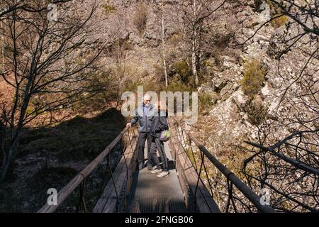 Liebevoller älterer Mann und Frau, die einander angucken, während sie auf einer Fußgängerbrücke gegen felsige Berge stehen Stockfoto