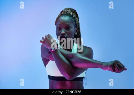 Junge afroamerikanische Sportlerin in Sportkleidung beim Sport Beim Blick auf blauen Hintergrund Stockfoto