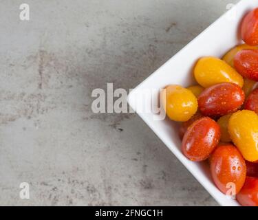 Rote und gelbe kleine Tomaten in einer weißen quadratischen Schüssel. Flach liegend Stockfoto