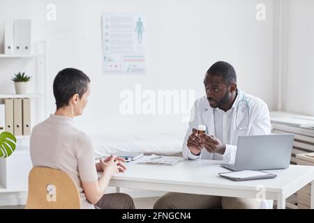 Afrikanischer junger Arzt verschreibt die Medizin der Frau, während sie sie Sitzen am Tisch im Büro Stockfoto